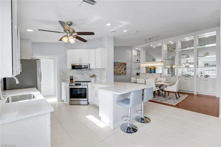 Kitchen featuring a kitchen bar, stainless steel appliances, white cabinetry, a peninsula, and ceiling fan