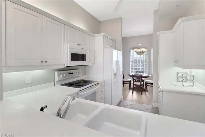 Kitchen featuring white appliances, white cabinets, light countertops, and decorative light fixtures