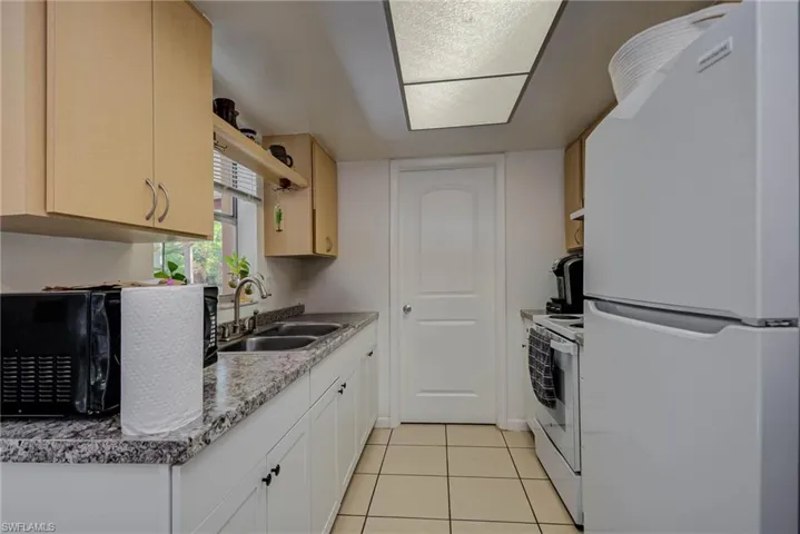 Kitchen featuring a sink, light tile patterned floors, white appliances, and white cabinetry