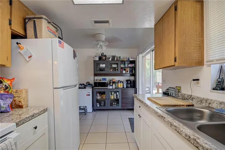 Kitchen with a ceiling fan, visible vents, light tile patterned floors, light countertops, and freestanding refrigerator