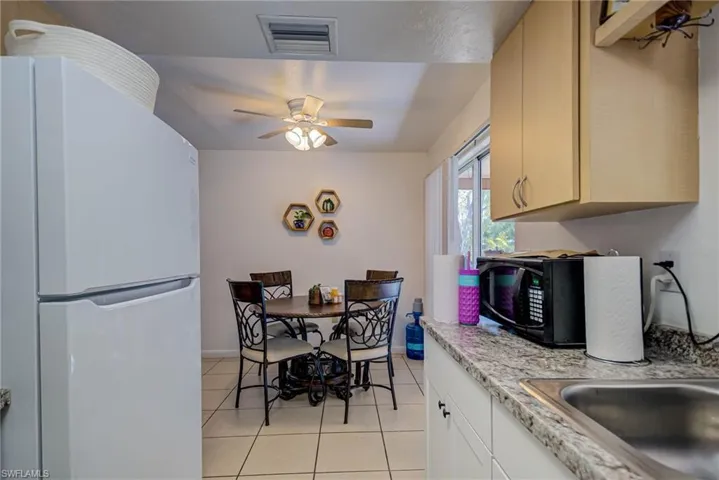 Kitchen featuring light tile patterned flooring, ceiling fan, black microwave, freestanding refrigerator, and visible vents