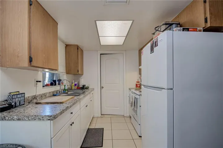 Kitchen featuring a sink, light tile patterned floors, white appliances, and light countertops