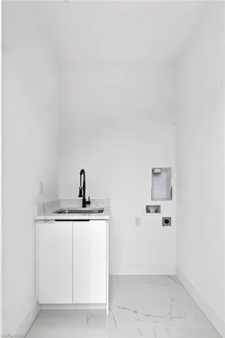 Utility room featuring a white single-basin sink with a matte black faucet, white cabinetry, a quartz countertop, and white tile flooring with veining