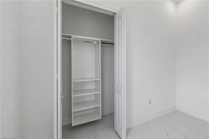 Interior closet with built-in shelving unit, clothing rod, bi-fold door, white baseboards, and marble-look tile flooring