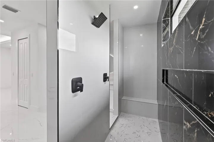 Walk-in shower featuring matte black fixtures, white tile wall, and contrasting dark marbled wall with an integrated niche