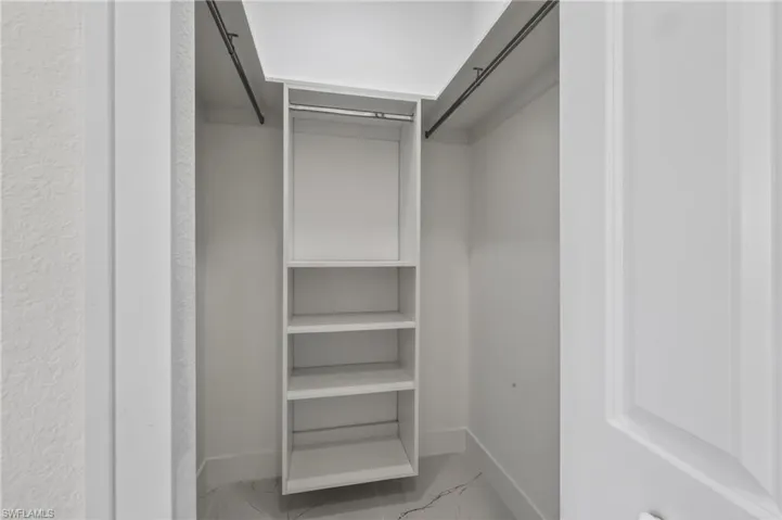 Closet organization system featuring built-in shelving, hanging rods, white paneling, and a white baseboard