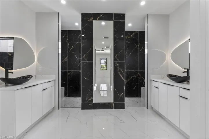 Dual vanities featuring white cabinetry and countertops, vessel sinks, and backlit mirrors