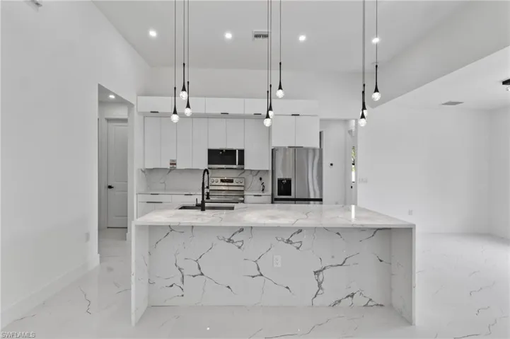 Modern kitchen featuring a waterfall island with veined quartz countertops, white cabinetry, stainless steel appliances, and sleek pendant lighting