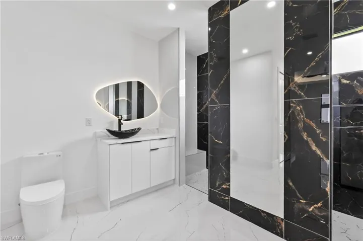 Modern bathroom featuring a white vanity with a rectangular countertop, a vessel sink, and a backlit irregular-shaped mirror