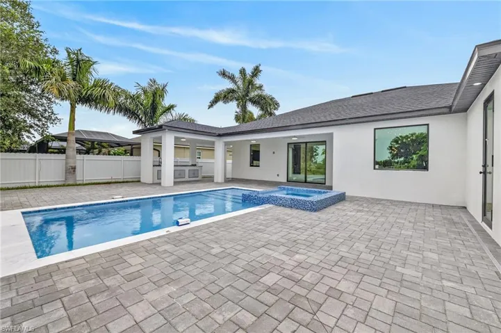 Expansive paver patio with a rectangular swimming pool, integrated spa, and covered outdoor kitchen