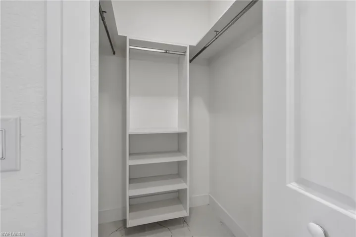 Walk-in closet featuring built-in shelving, two hanging rods, white walls, and a light-toned flooring