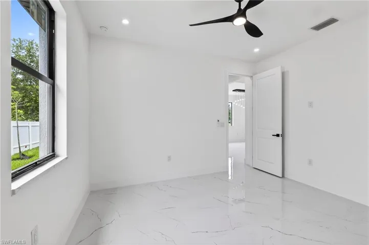 Spacious room featuring large format marble-look tile flooring, a modern black ceiling fan, recessed lighting, white walls, and a contemporary interior door with black hardware
