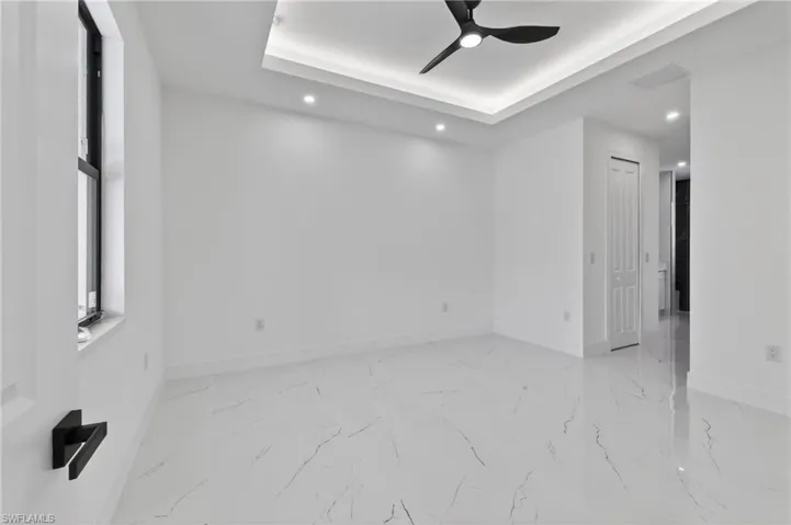 Spacious room featuring white tile flooring, a tray ceiling with recessed lighting, and a modern ceiling fan