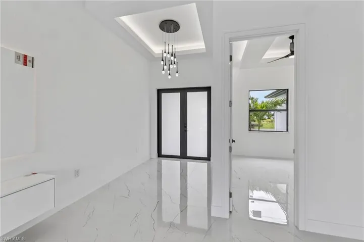 Entryway featuring large format tile flooring, a modern chandelier with multiple pendants, and tray ceiling with recessed lighting