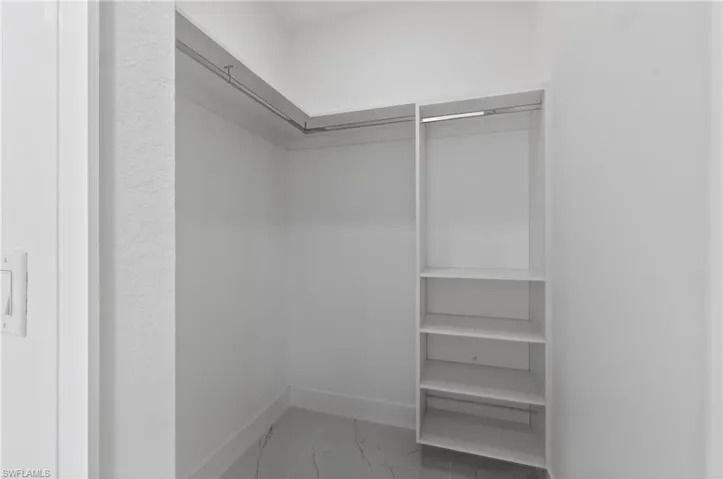 Walk-in closet featuring white walls, baseboards, marble-look tile flooring, chrome hanging rods, and integrated shelving