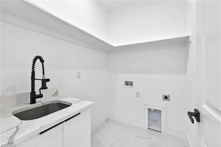 Dedicated laundry space featuring a matte black pull-down faucet, undermount sink, stone-finish countertop, white cabinetry with linear pulls, and coordinated tile flooring