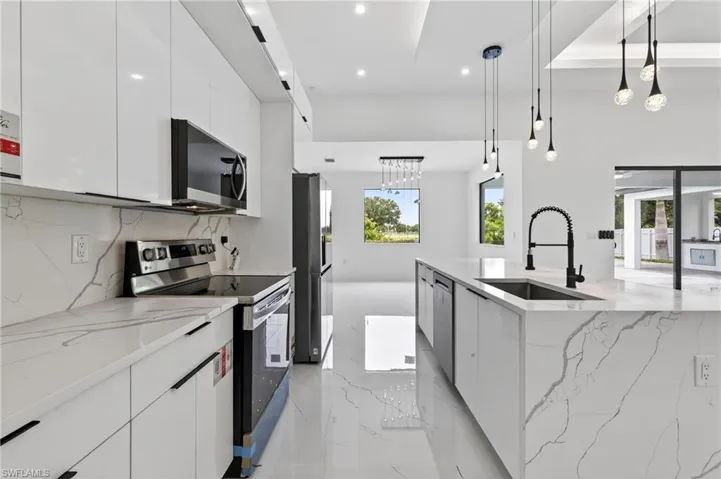 Modern kitchen featuring a waterfall island with an undermount sink and matte black faucet, stainless steel appliances, white flat-panel cabinetry, and polished tile flooring