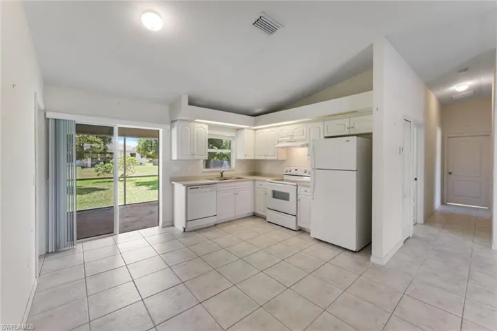 Kitchen with white appliances, lofted ceiling, light countertops, light tile patterned floors, and white cabinets