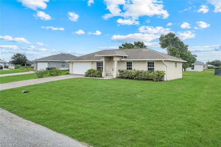 Ranch-style house with driveway, stucco siding, a front lawn, a garage, and a shingled roof