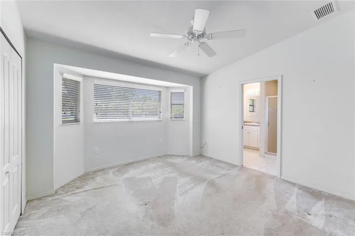 Unfurnished bedroom with lofted ceiling, light carpet, a closet, ensuite bath, and ceiling fan