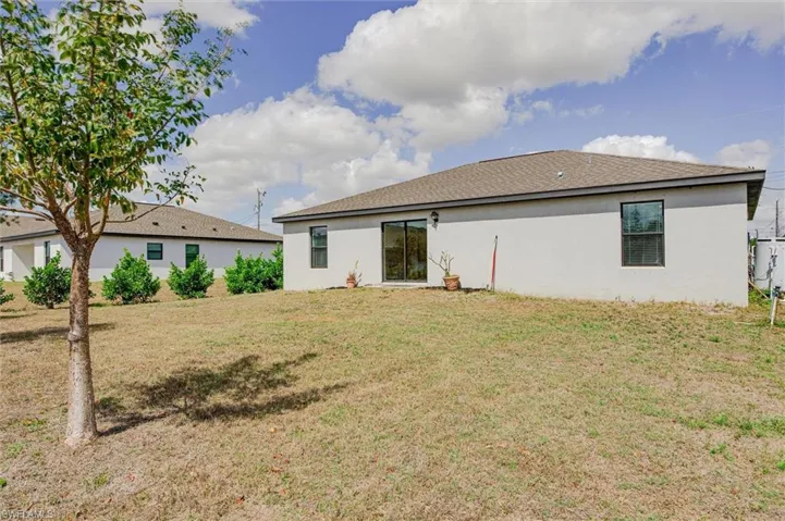Back of house featuring a yard, a shingled roof, and stucco siding