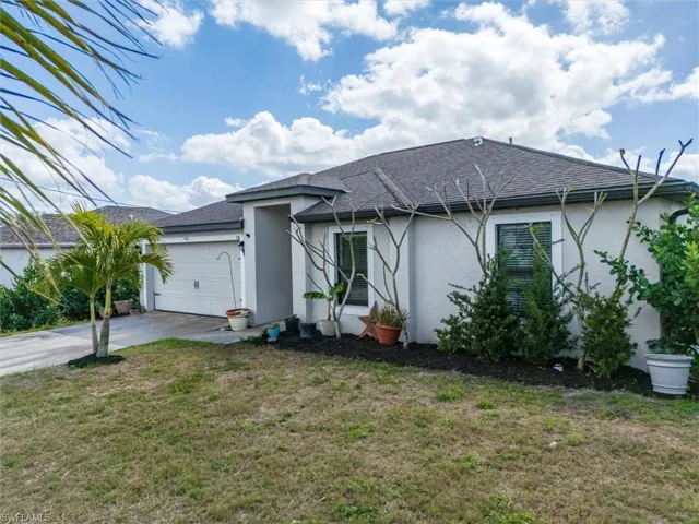 Ranch-style home featuring roof with shingles, a front lawn, an attached garage, stucco siding, and concrete driveway