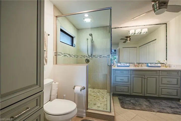 Bathroom featuring vanity, tiled shower, a ceiling fan, and tile patterned floors