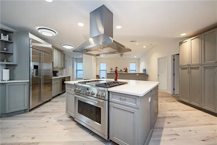 Kitchen with gray cabinetry, high end appliances, island exhaust hood, light wood-type flooring, and healthy amount of natural light