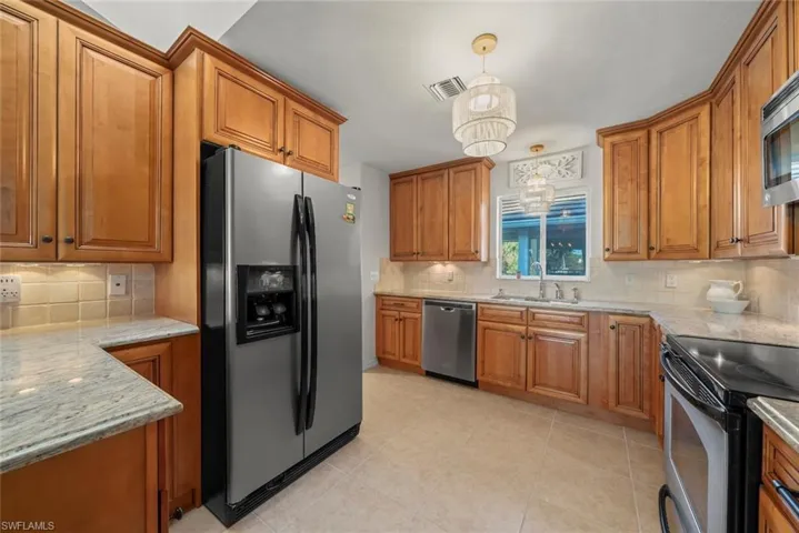 Kitchen with stainless steel appliances, light brown cabinetry, light granite countertops, and tasteful backsplash