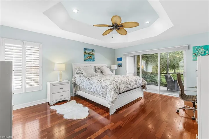 Tray ceiling with recessed lighting and a ceiling fan, wood-finish flooring, sliding glass doors to a screened patio, and window with plantation shutters