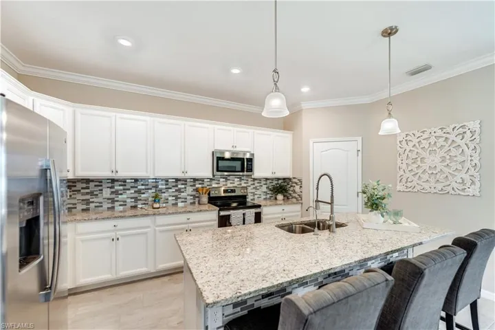 Kitchen featuring appliances with stainless steel finishes, a kitchen island with sink, sink, white cabinetry, and light stone counters