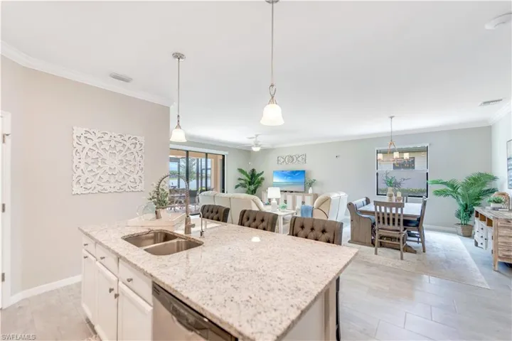 Kitchen featuring light stone countertops, a center island with sink, pendant lighting, ornamental molding, and ceiling fan