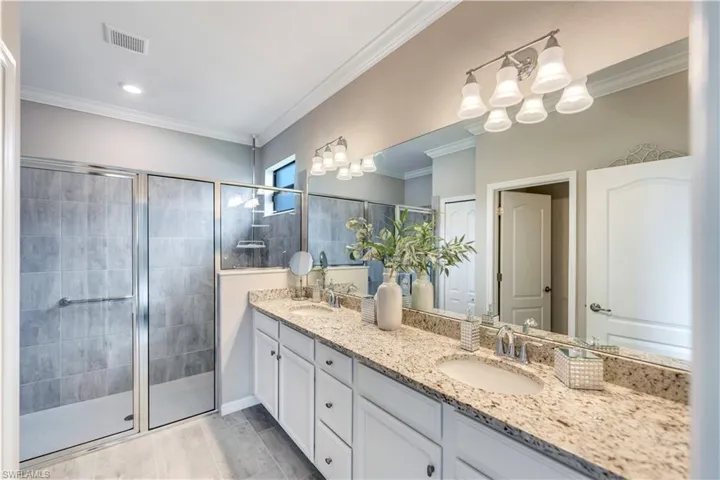 Bathroom featuring crown molding, vanity, a shower with shower door, and an inviting chandelier