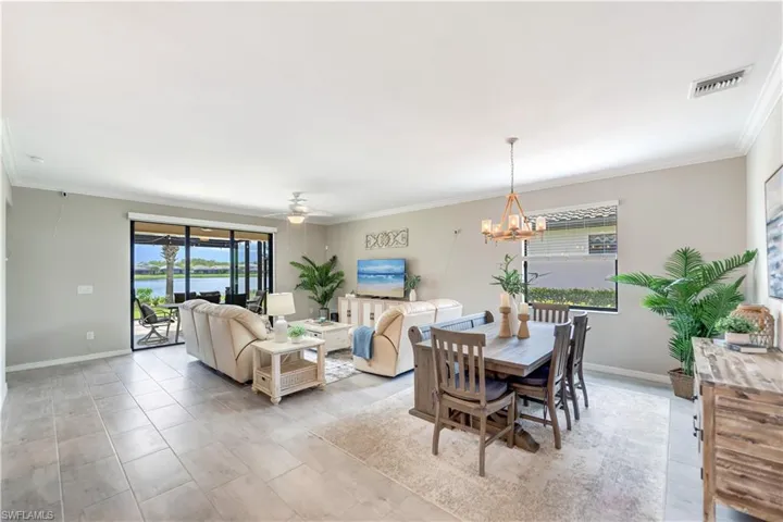 open concept living space featuring light tile patterned floors, ornamental molding, and ceiling fan with notable chandelier
