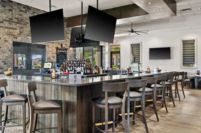 Bar featuring ceiling fan, stainless steel counters, and light hardwood / wood-style floors