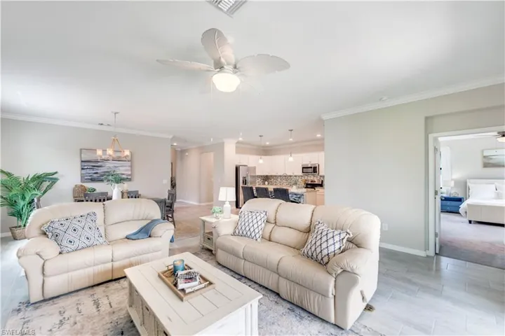 Carpeted living room featuring ceiling fan with notable chandelier and crown molding