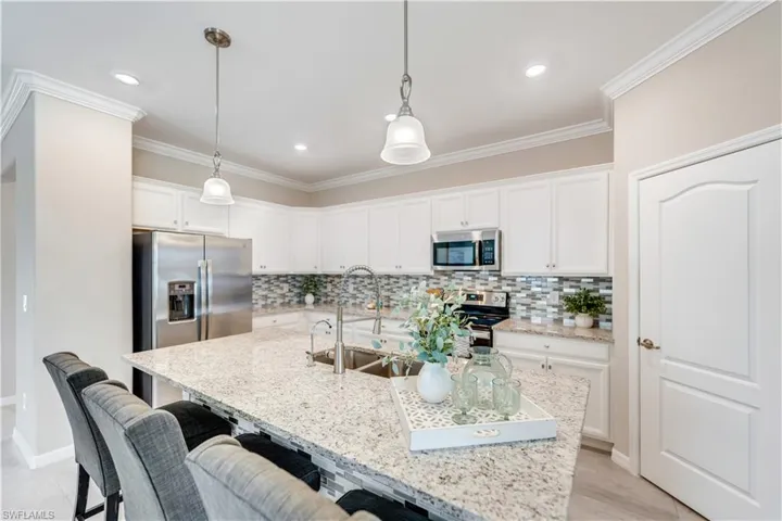 Kitchen with a kitchen island with sink, stainless steel appliances, a kitchen breakfast bar, light stone counters, and sink