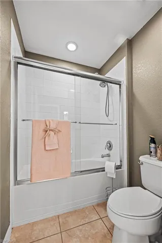 Bathroom featuring shower / bath combination with glass door, toilet, and tile patterned floors