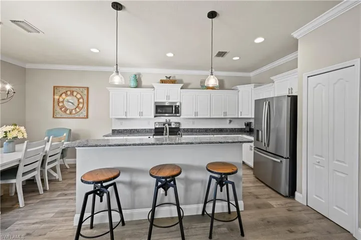 Kitchen featuring decorative light fixtures, white cabinetry, stainless steel appliances, a center island with sink, and light hardwood / wood-style floors