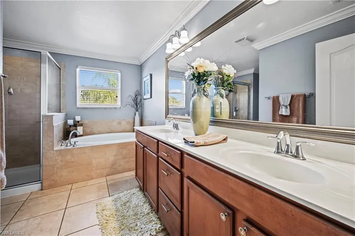 Bathroom with double vanity, independent shower and bath, tile patterned floors, and crown molding