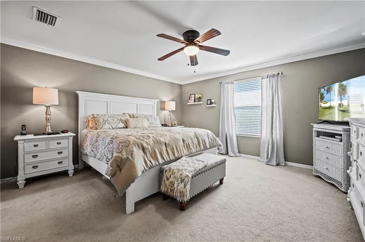 Carpeted bedroom featuring multiple windows, ceiling fan, and ornamental molding