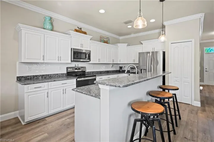 Kitchen featuring appliances with stainless steel finishes, white cabinetry, hardwood / wood-style flooring, and an island with sink