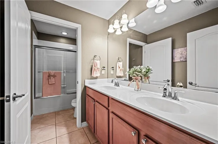 Full bathroom with dual vanity, toilet, tile patterned floors, and combined bath / shower with glass door