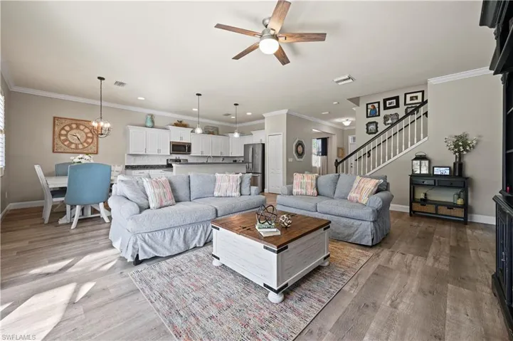 Living room featuring light hardwood / wood-style floors, ceiling fan with notable chandelier, and crown molding