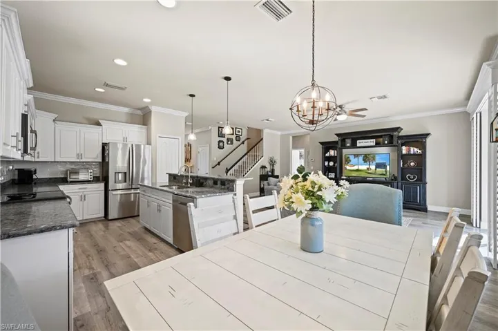 Dining area featuring ceiling fan with notable chandelier, light hardwood / wood-style floors, sink, and ornamental molding