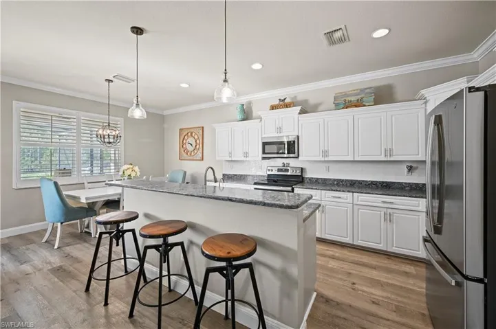 Kitchen featuring pendant lighting, white cabinets, light wood-type flooring, a center island with sink, and appliances with stainless steel finishes