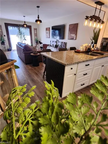 Kitchen featuring light stone counters, decorative light fixtures, open floor plan, white cabinetry, and a sink