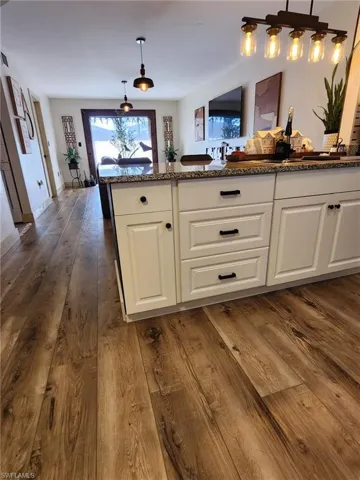 Kitchen with stone counters, white cabinets, decorative light fixtures, and dark wood-style flooring