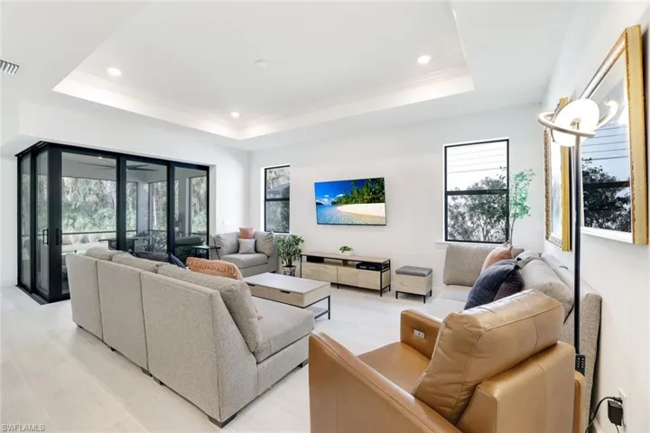 Spacious living area featuring a tray ceiling with recessed lighting, large sliding glass doors, white walls, and light-toned flooring