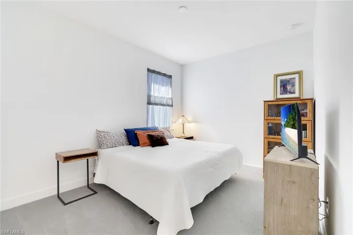 Carpeted bedroom featuring white walls and a window with sheer drapes